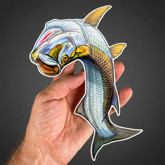 Leaping Tarpon vinyl sticker held between fingers, Silver King fly fishing decal on a dark background