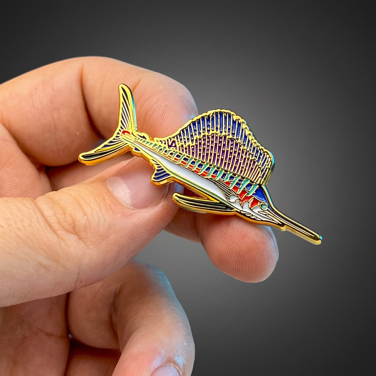 Gold Sailfish pin held in hand against a dark background
