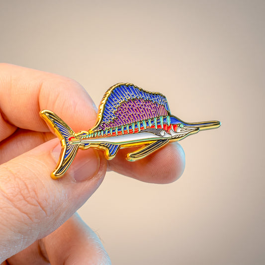 Macro close-up of gold Sailfish pin held in hand