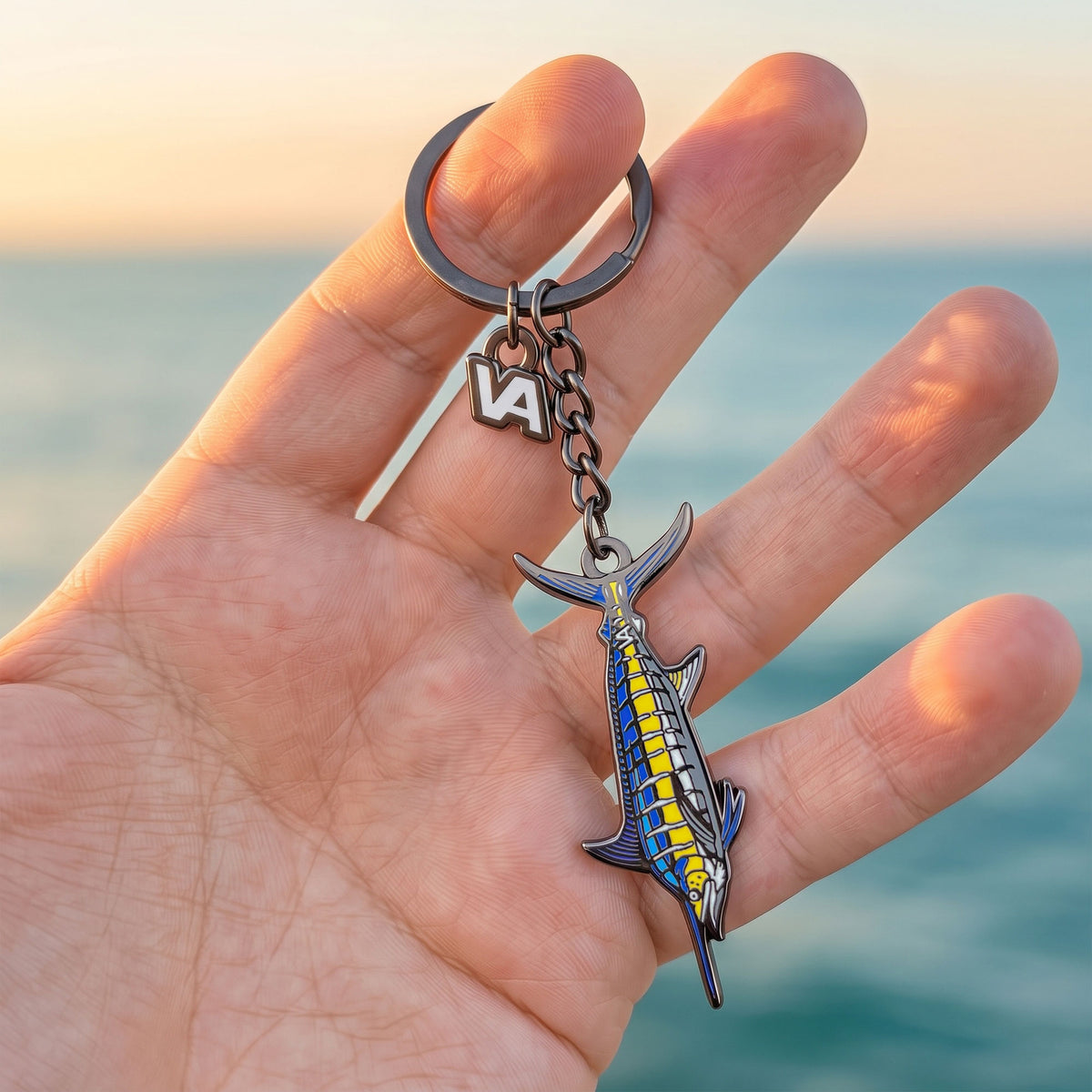 Blue Marlin keychain held in hand with the ocean at sunset in the background