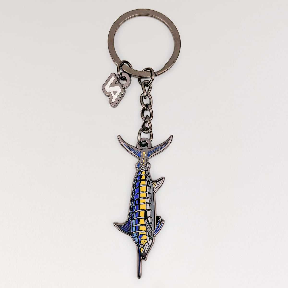Blue Marlin keychain, black nickel hard enamel charm with the VEDUTA DESIGN VA logo charm and chain, on a light studio background