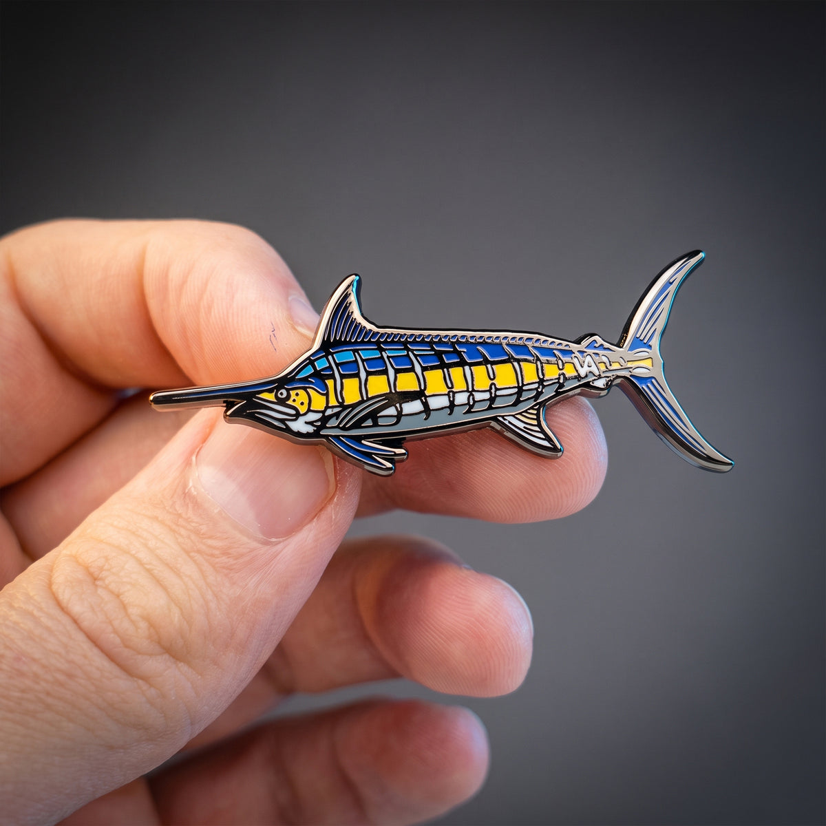 Blue Marlin pin held in hand against a dark background