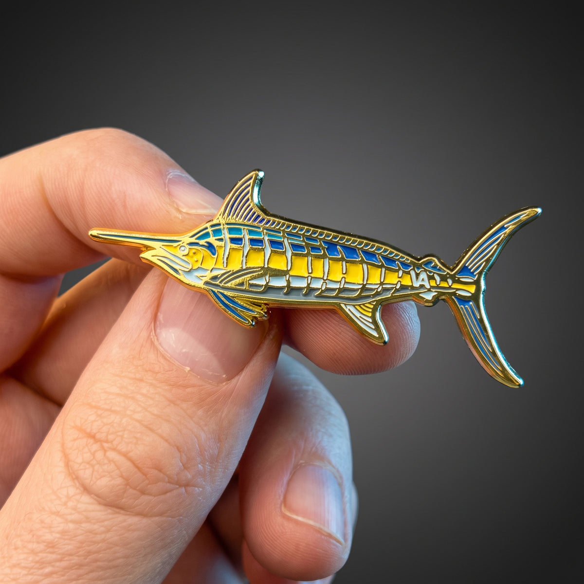 Blue Marlin pin held in hand against a dark background