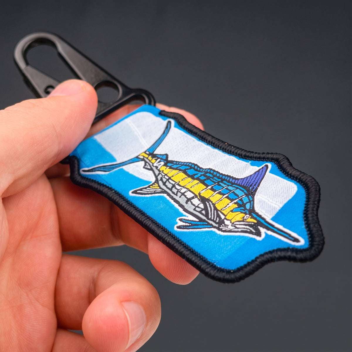 Blue Marlin woven keychain held in hand against a dark background