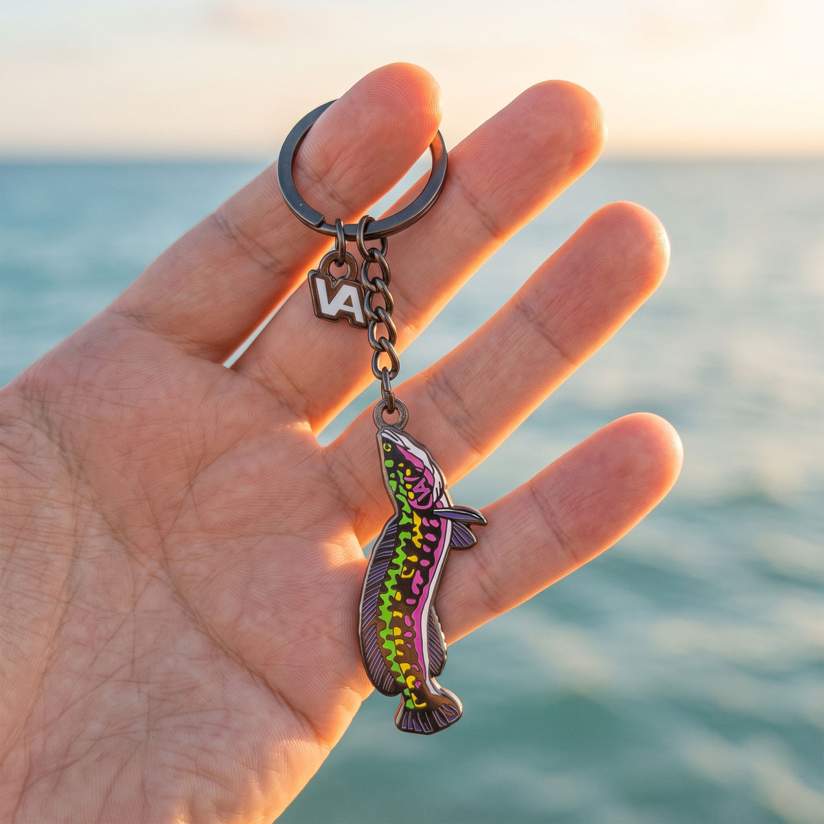 Giant Snakehead keychain held in hand with the ocean at sunset in the background