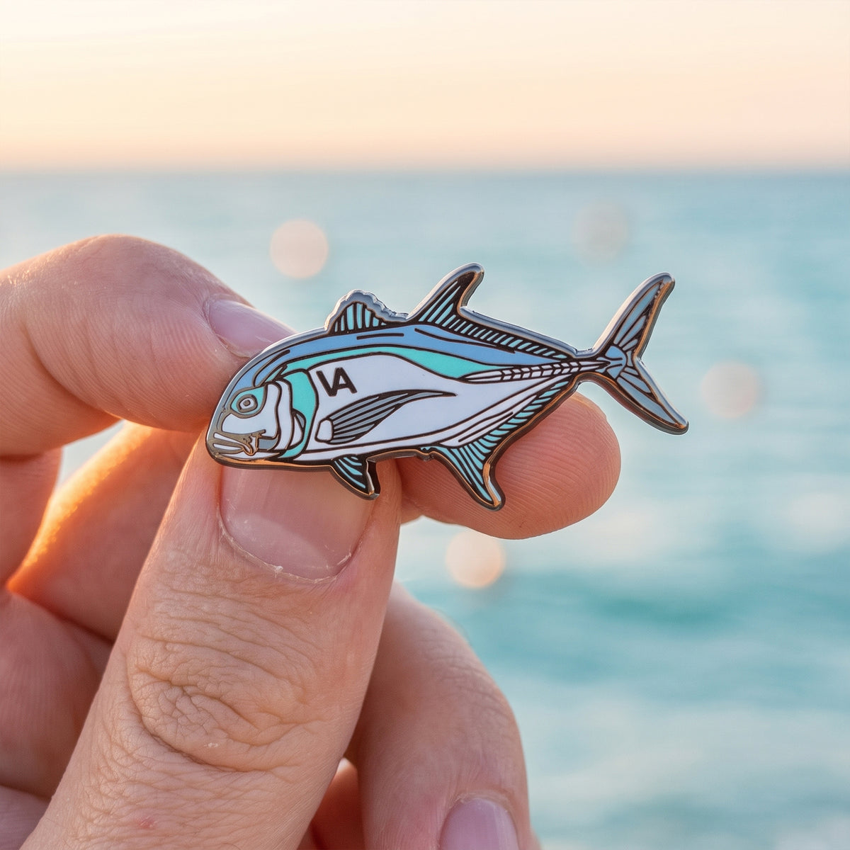 Giant Trevally pin held in hand with ocean and sunset in the background