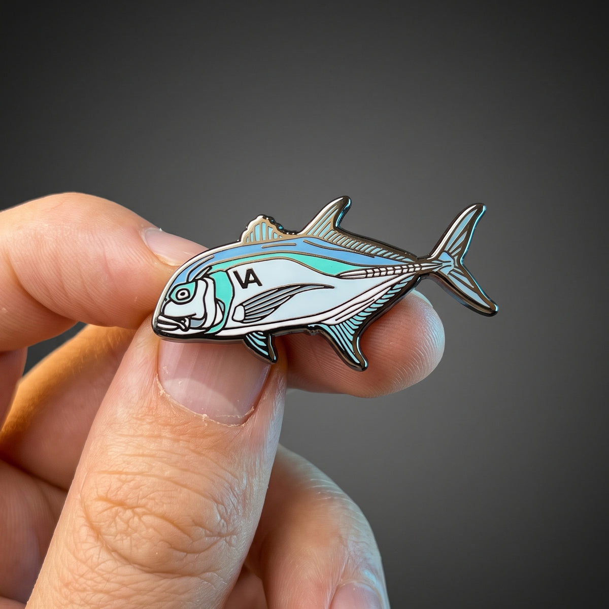 Giant Trevally pin held in hand against a dark background
