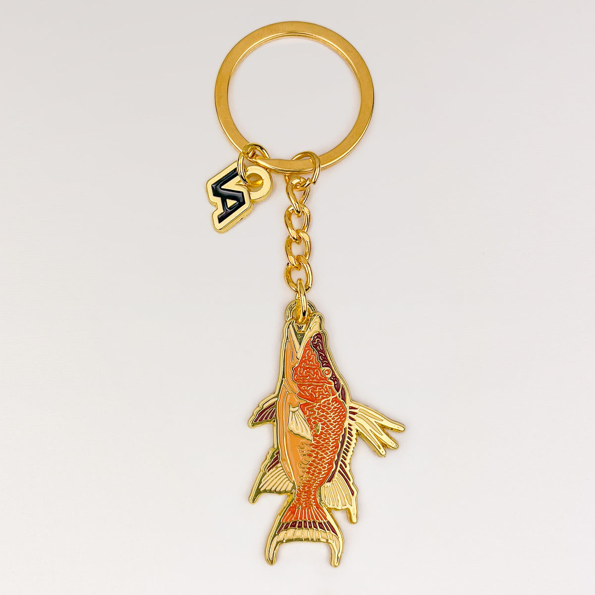 Hogfish keychain, gold soft enamel charm with the VEDUTA DESIGN VA logo charm and chain, on a light studio background
