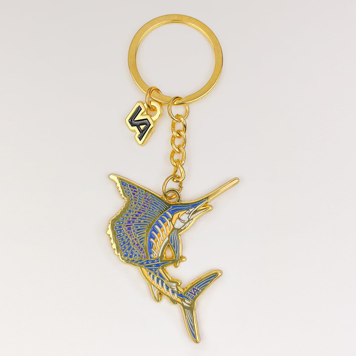 Leaping Sailfish keychain, gold soft enamel charm with the VEDUTA DESIGN VA logo charm and chain, on a light studio background