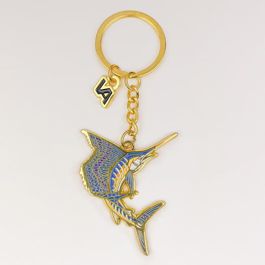 Leaping Sailfish keychain, gold soft enamel charm with the VEDUTA DESIGN VA logo charm and chain, on a light studio background