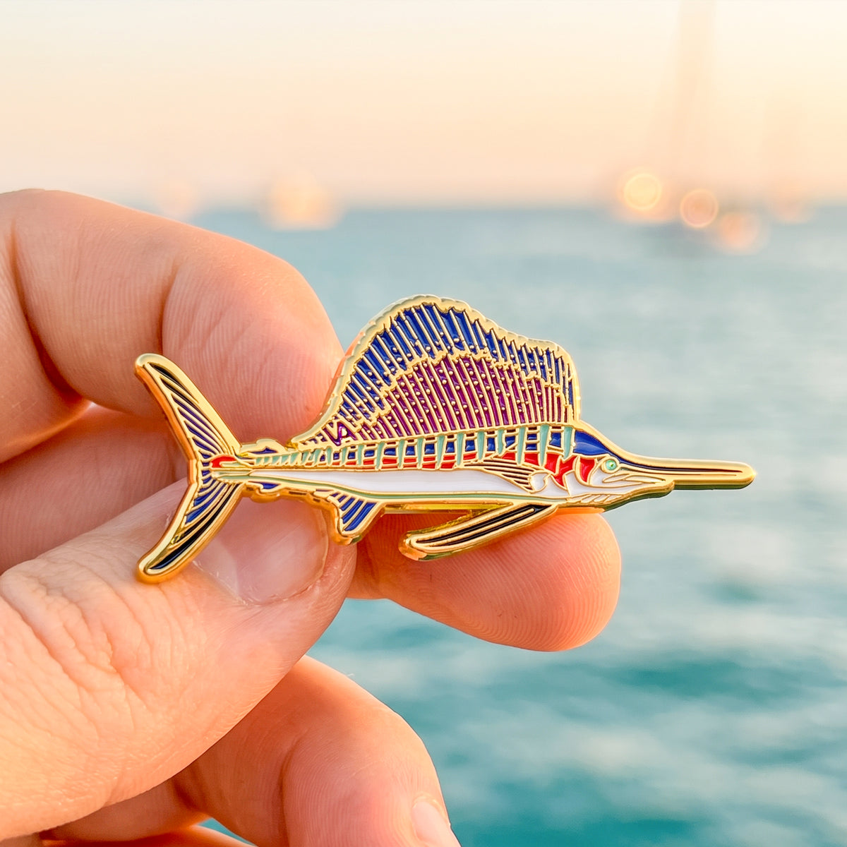Sailfish pin held in hand with a marina and ocean in the background