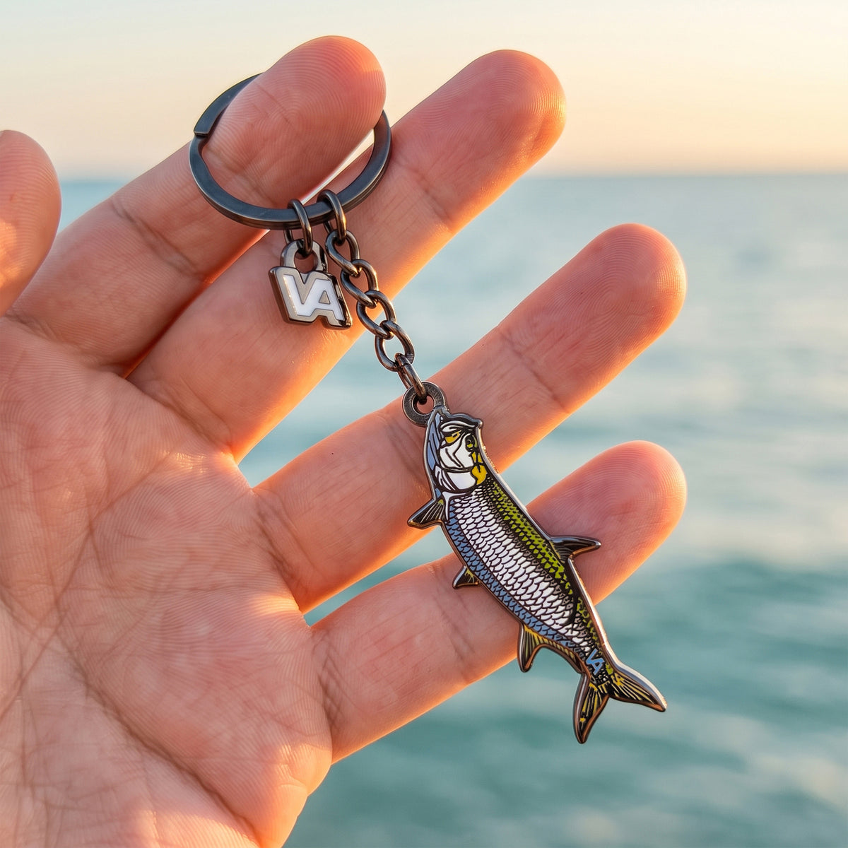 Tarpon keychain held in hand with the ocean at sunset in the background