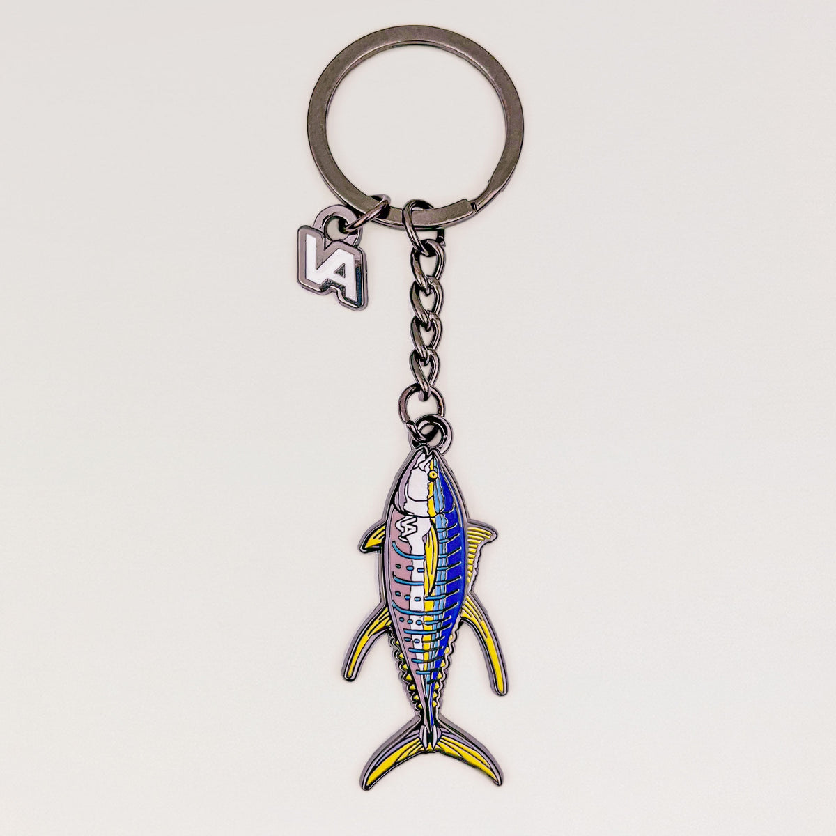 Yellowfin Tuna keychain, black nickel hard enamel charm with the VEDUTA DESIGN VA logo charm and chain, on a light studio background